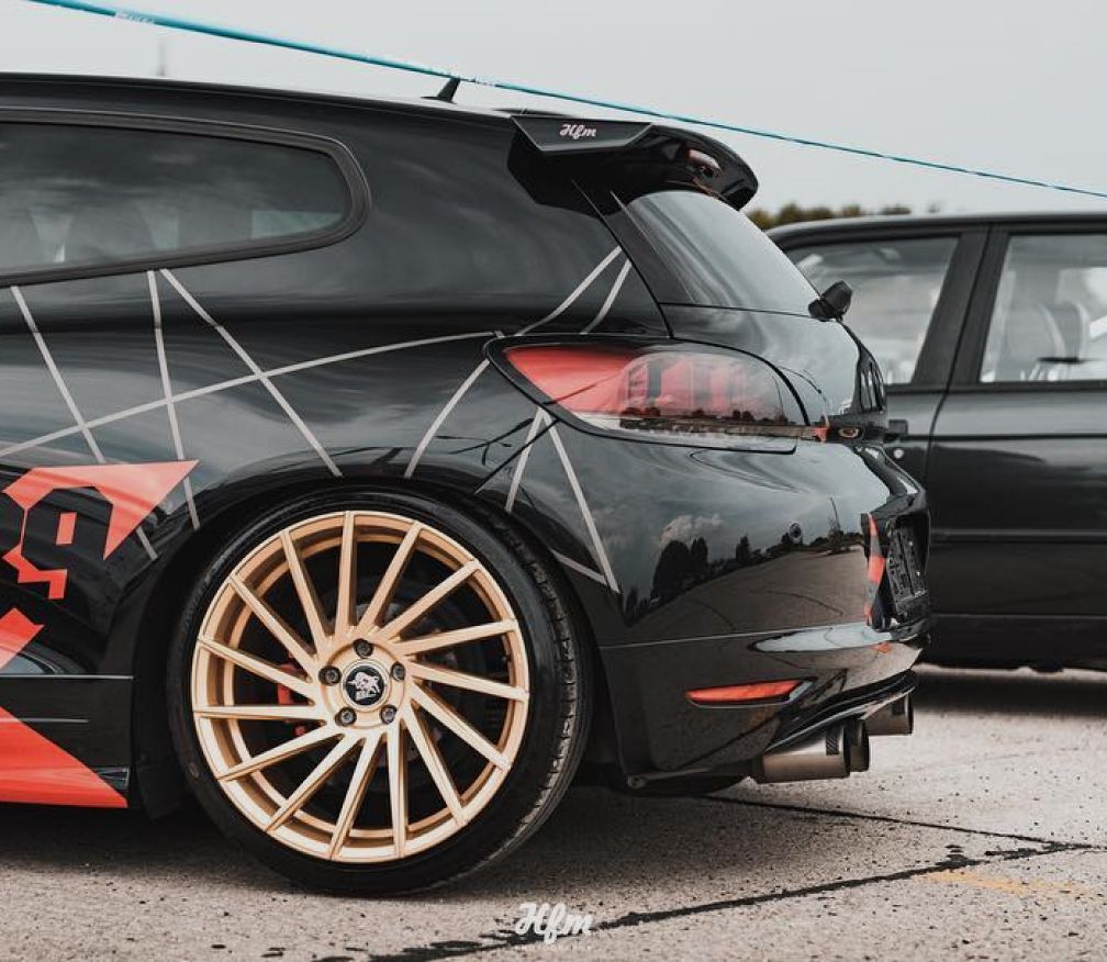 Heck eines dunklen Wagens mit goldenen Felgen und Designfolierung
